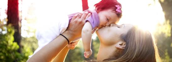 Kuva naisesta suukottamassa ja nostamassa vauvaa.