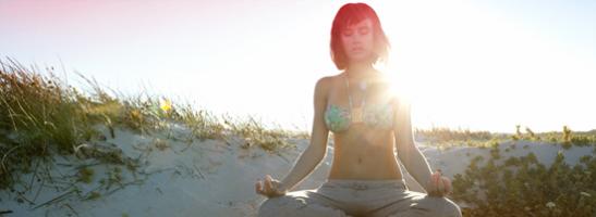 Kuva naisesta istumassa rannalla meditoimassa. Kuva kuvastaa, että on mahdollista rentoutua kuukautistenkin aikana. 